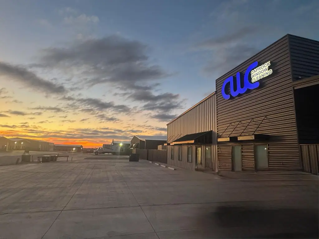 The Caprock Window Cleaning shop building at sunset, its illuminated blue CWC sign lit against an orange West Texas sky