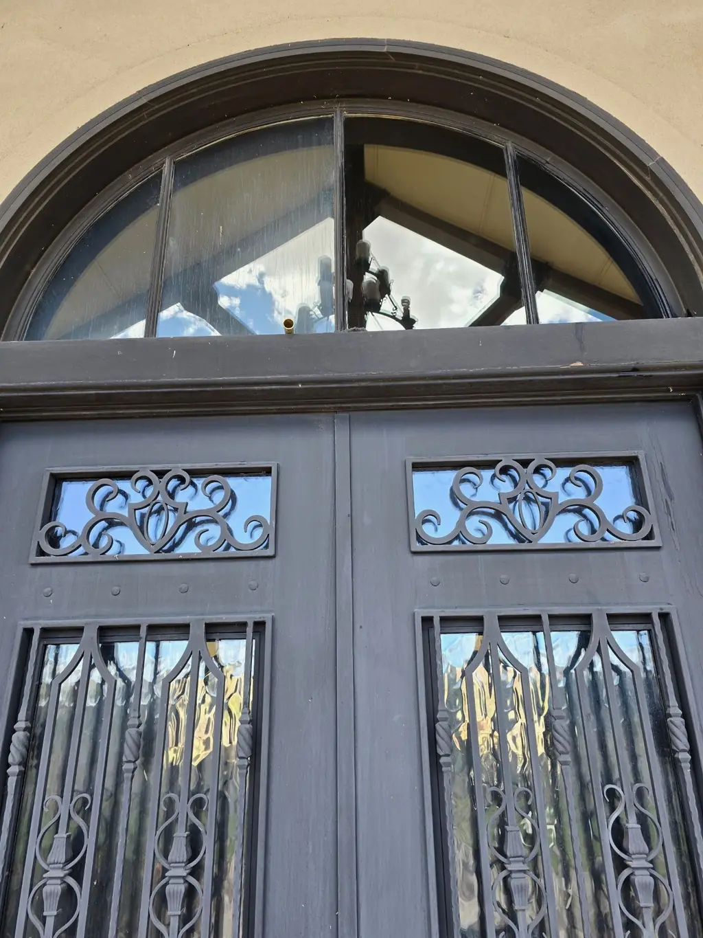An ornate arched wrought-iron-and-glass double entry door, spotless, after cleaning