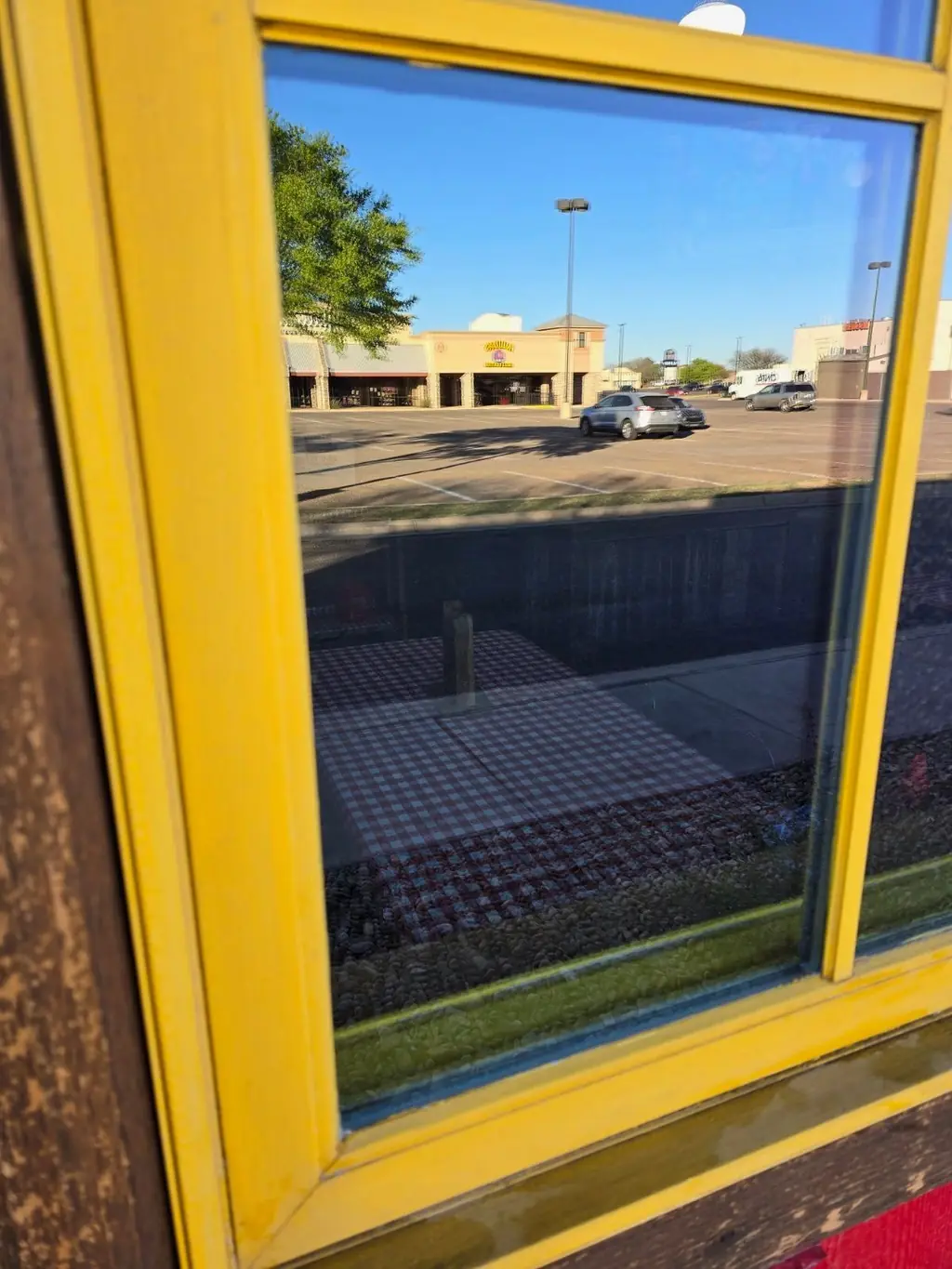 The same yellow-framed storefront window after cleaning, the glass clear and holding a sharp reflection of the parking lot