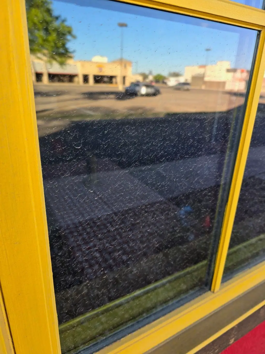 A yellow-framed storefront window covered edge to edge in hard water spotting